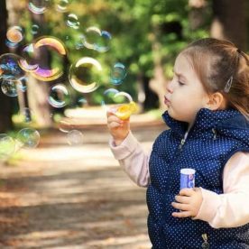 A little girl blows bubbles through a bubble wand.