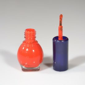 Open red nail polish sitting on a white table.