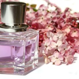 A perfume bottle in front of lilac flowers.