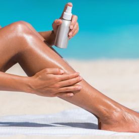 A woman spreading tanning oil across her calf on the beach.