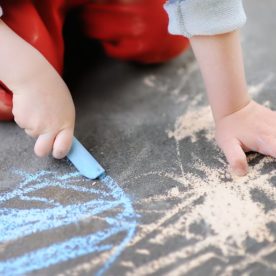 A kid draws on the sidewalk with blue chalk.