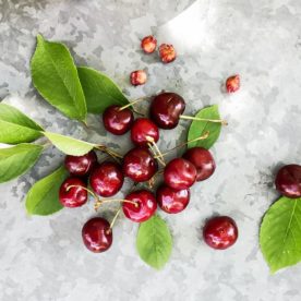 Fresh cherries and their fruit pits sitting on a marble table.
