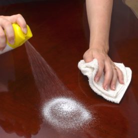Someone using furniture polish spray on a hardwood table.