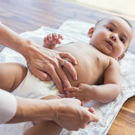 A mother replaces a baby's diaper with feces with a new diaper.