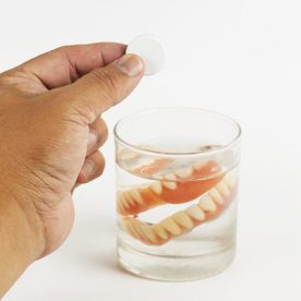 someone with dentures in a glass about to add denture cleansers