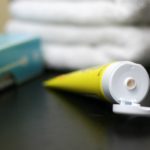 A tube of diaper cream sits open besides a stack of diapers on a changing table.