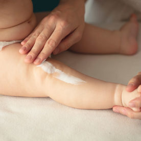 A parent applying baby lotion to their baby's leg.
