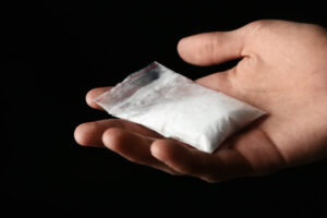 Drug dealer holding bag with cocaine on black background, closeup