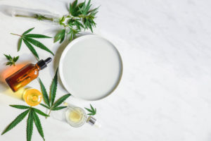 Various glass bottles with CBD oil, THC tincture and hemp leaves on a marble background.