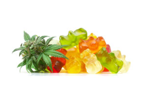 CBD-infused gummies bears stack atop each other with a small clump of marijuana leaves beside them.
