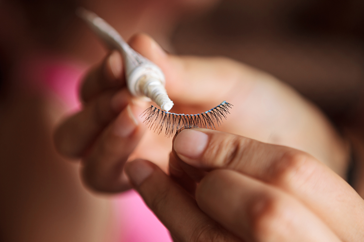 Hands holding a temporary eyelash in one hand while dabbing eyelash glue on the edges.