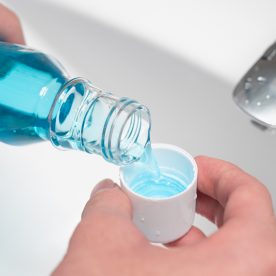 A man poring blue mouth wash with carbamide peroxide into the cap over a sink.