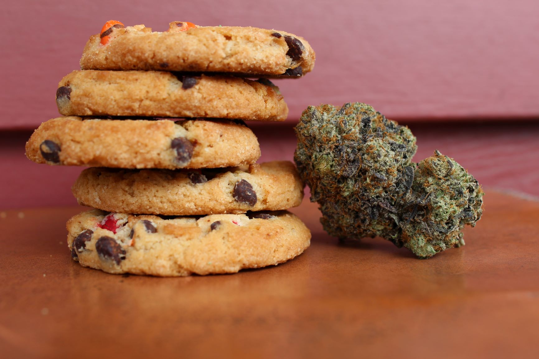 A stack of chocolate chip cookies infused with cannabis besides a nugget of cannabis.