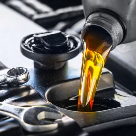 Motor oil being poured into a car's oil canister with a wrench besides it.