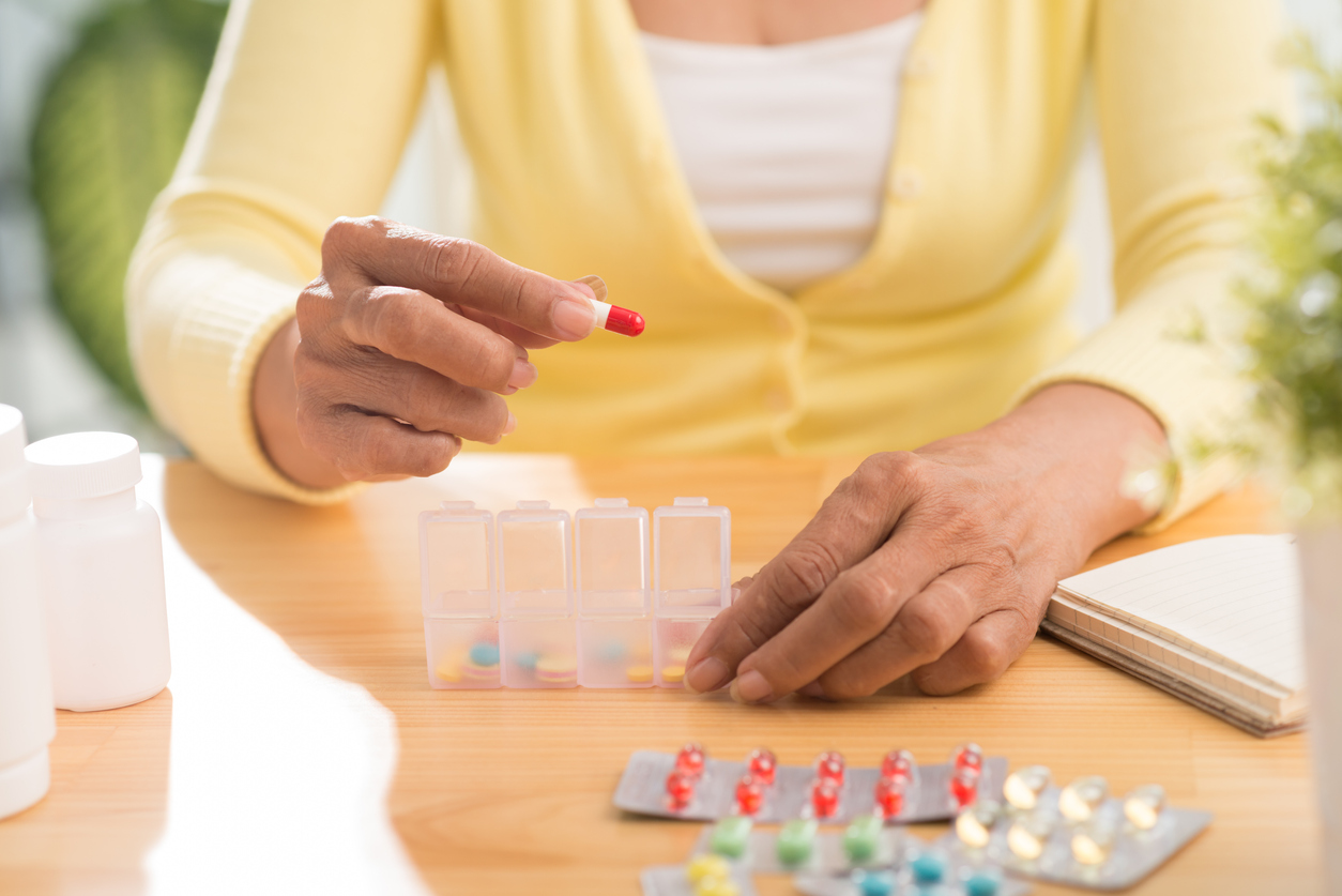 Older adult handling medications with a weekly pill organizer and blister packs on a table