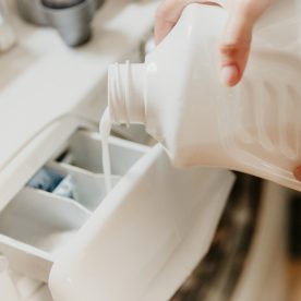 Someone pouring liquid laundry detergent into washing machine.