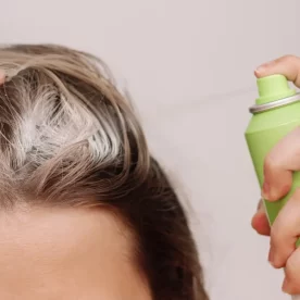 Woman sprays dry shampoo on her scalp