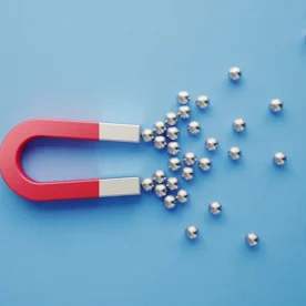 A red and silver, U-shaped, high-power magnet draws in small, magnetic balls.