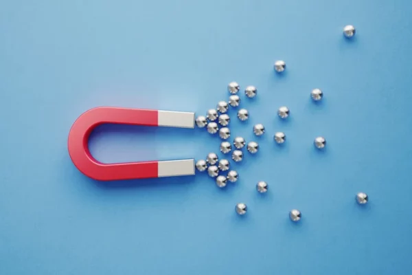 A red and silver, U-shaped, high-power magnet draws in small, magnetic balls.