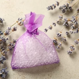 A purple sachet filled with scent boosting beads. It's laying on a flat surface surrounded by lavender sprigs.