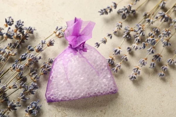 A purple sachet filled with scent boosting beads. It's laying on a flat surface surrounded by lavender sprigs.