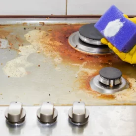 Bar Keepers friend powder on a purple sponge. Someone holds the sponge above a rusty stove.