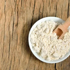 A bowl of colloidal oatmeal with a wooden scooper set on it. The bowl is resting on a wooden table.