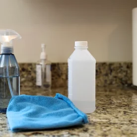 A bottle of rubbing alcohol on a counter next to a blue rag and a spray bottle.