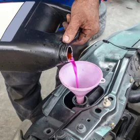A mechanic pours pink antifreeze into a car.