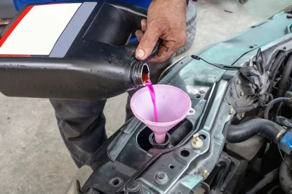 A mechanic pours pink antifreeze into a car.