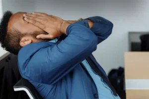 A man leans back in his chair and rubs his face in distress.