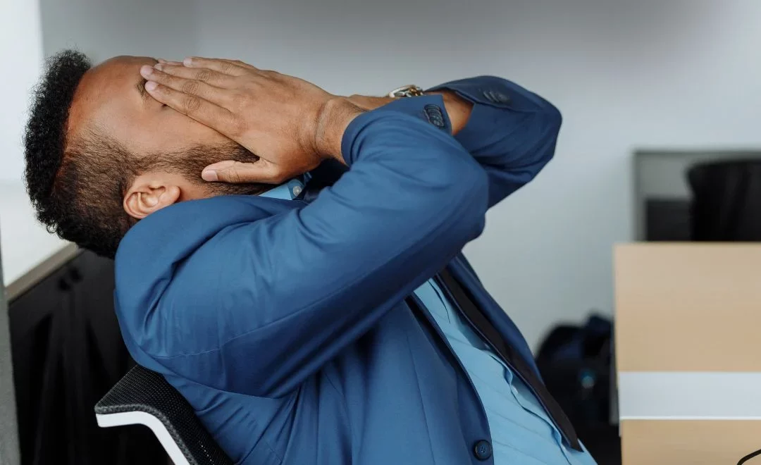 A man leans back in his chair and rubs his face in distress.