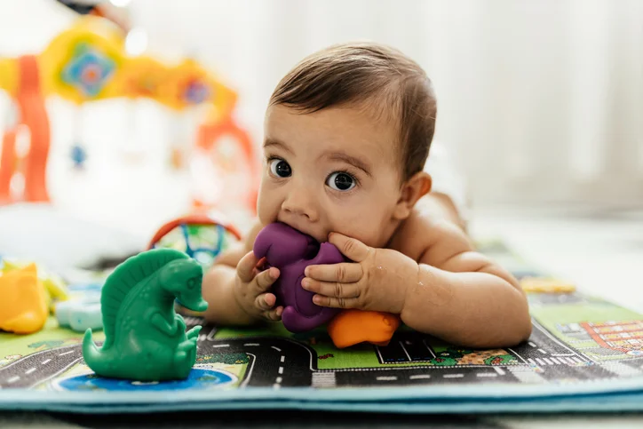 Baby playing with toys and is putting one in their mouth.
