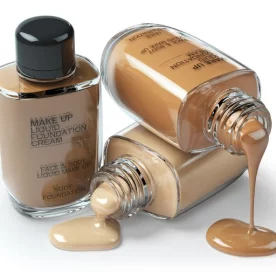 Three bottles of liquid foundation on a white background. Two are overturned and spilling.