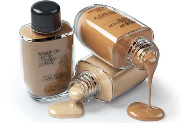 Three bottles of liquid foundation on a white background. Two are overturned and spilling.