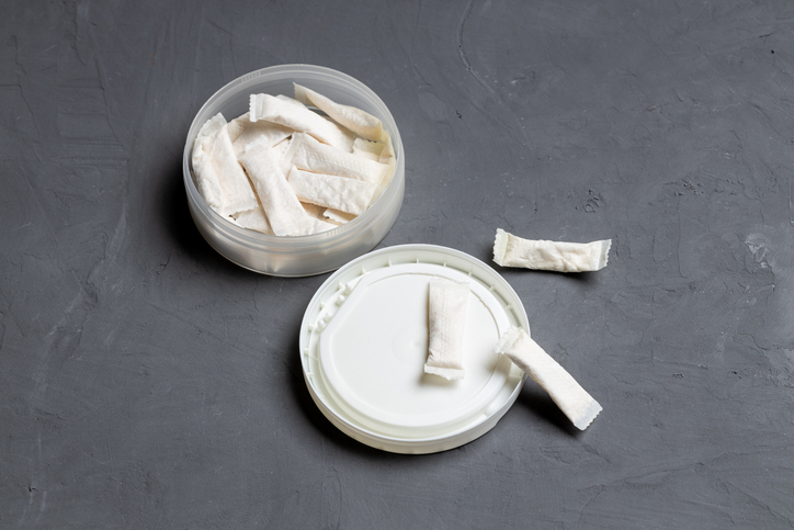 Nicotine pouches in a plastic container set on a gray background.
