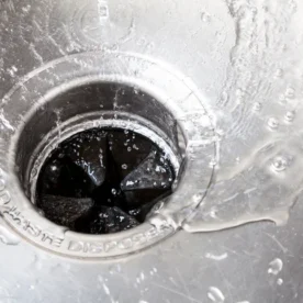 A closeup of a garbage disposal set in a metal sink. Water is running down into it.