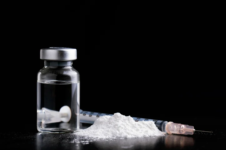 A vial with clear liquid next to white powder and an injector.